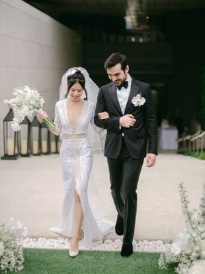 Bride in sequined gown with deep V-neck and groom in black tuxedo walking together after wedding ceremony.