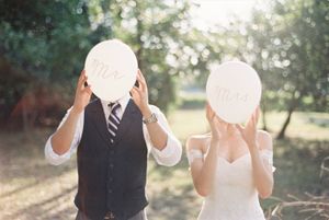 Bride and groom hold Mr. and Mrs. signs covering their faces at outdoor wedding.