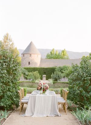 Romantic outdoor wedding reception table set in lush garden with French chateau backdrop.