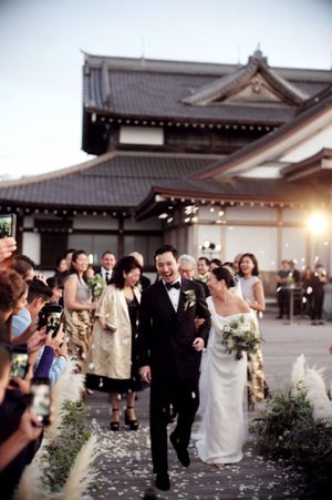 Joyful newlyweds exit ceremony at stunning Japanese temple venue with celebrating guests.