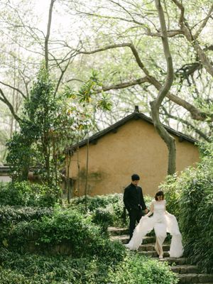 Bride and groom walk hand in hand up stone steps in lush garden setting.