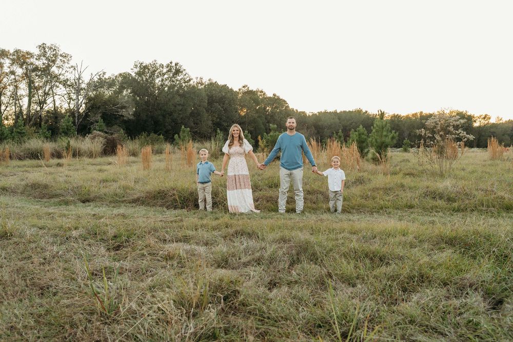 Family members walk together through a golden field at sunset wearing coordinated blue and white outfits.