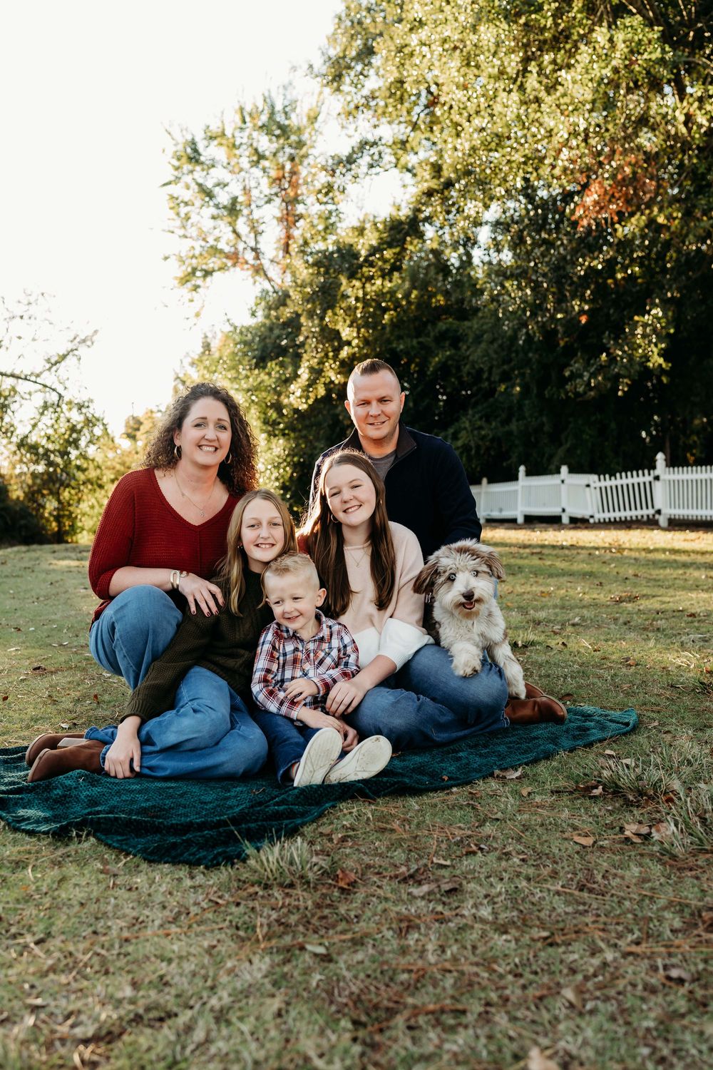 Family and their fluffy dog relaxing together on a blanket during an outdoor autumn photoshoot in a park.