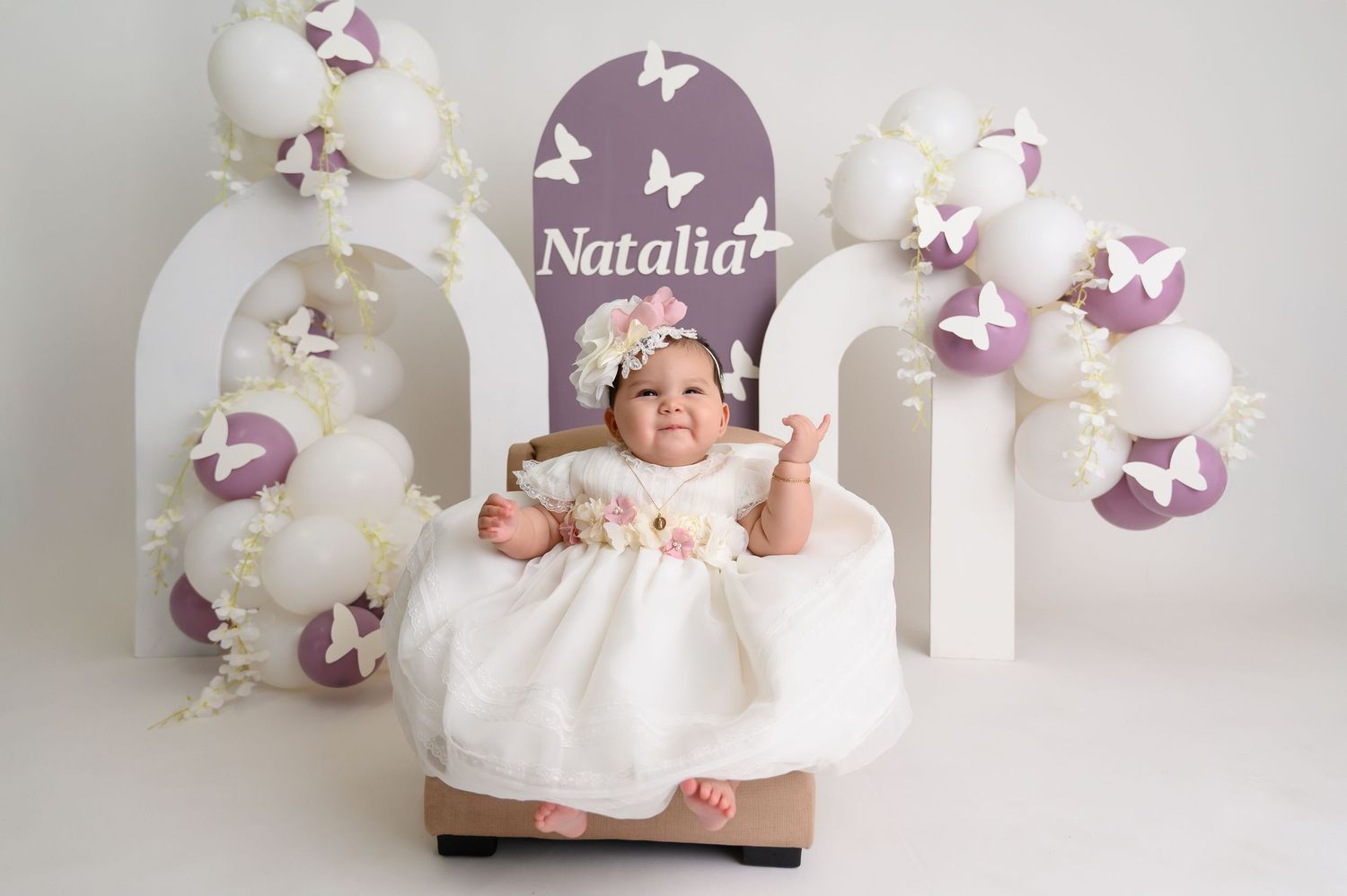 Dreamy baby photoshoot with purple butterflies and white floral decorations.