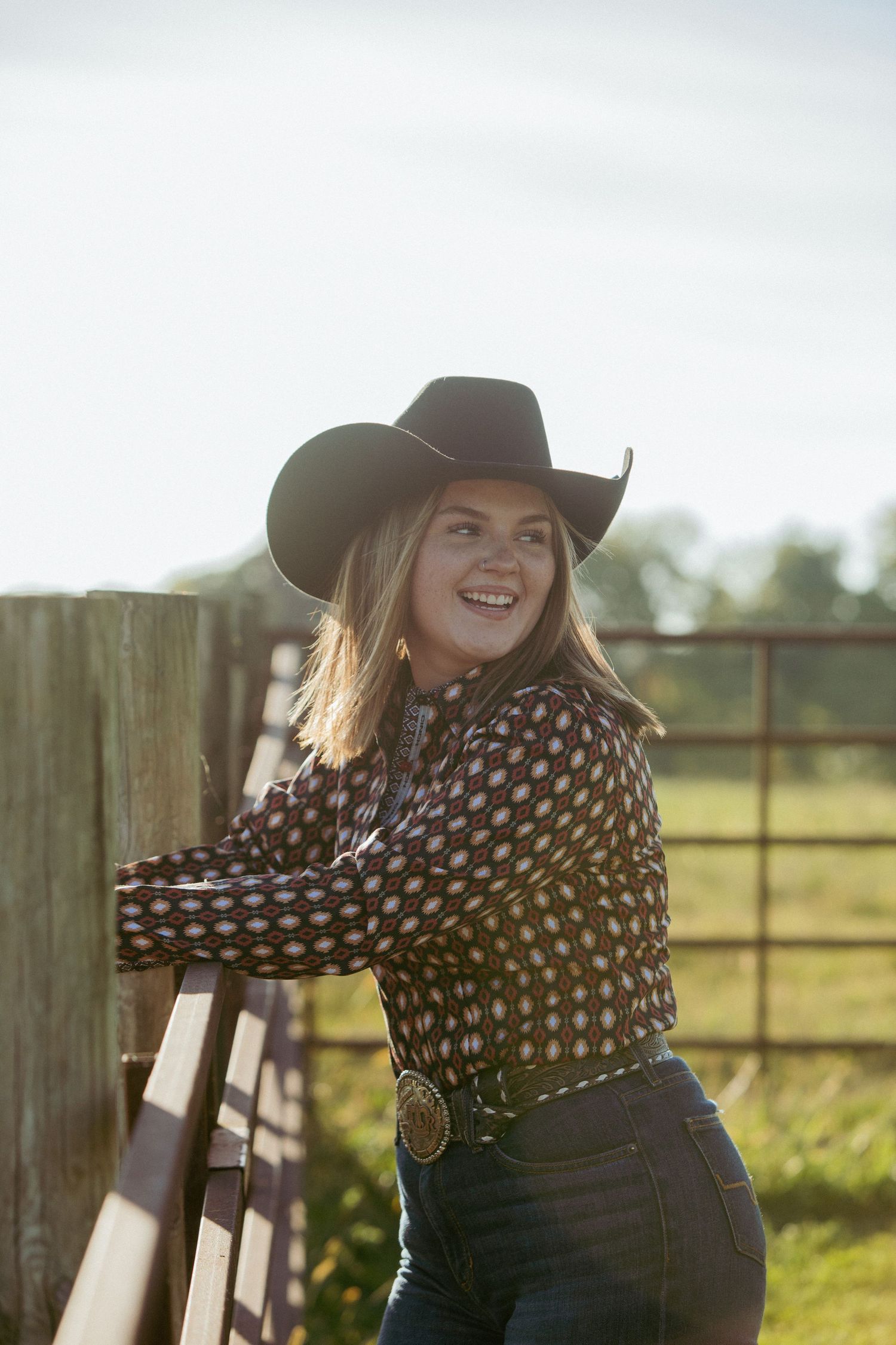 Rustic country scene with wooden fence and cowboy hat in warm sunlight.