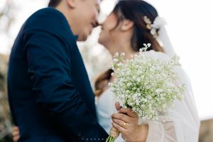 Elegant wedding scene with delicate baby's breath bouquet and couple in navy and white formal attire kissing.
