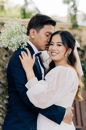 Romantic bridal couple embraces outdoors while holding baby's breath flowers at elegant wedding celebration.