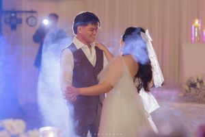 A couple shares their first dance at a wedding reception with soft lighting and fog on the dance floor.