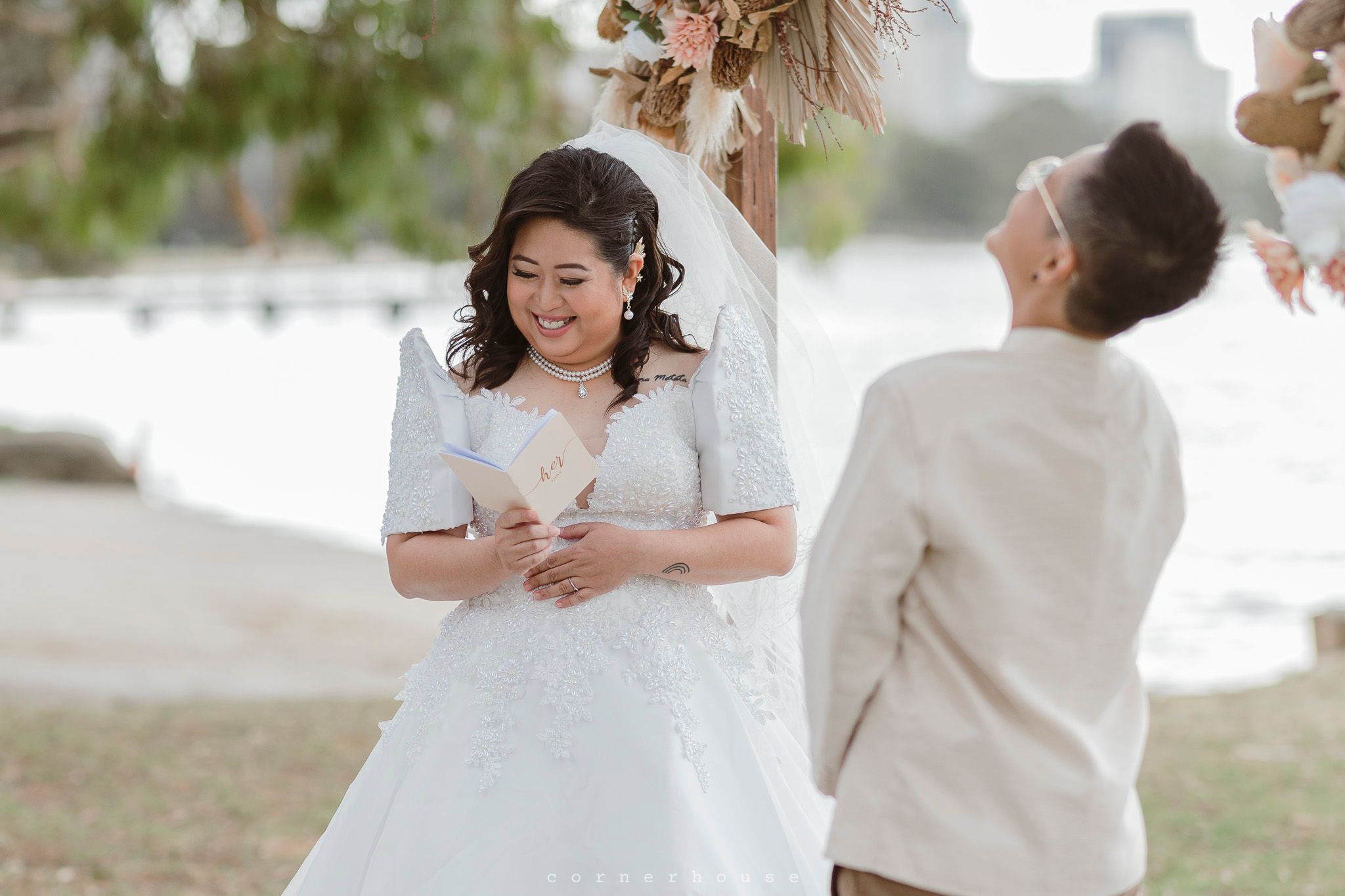 A bride in a white lace wedding dress reads her vows during an outdoor ceremony.