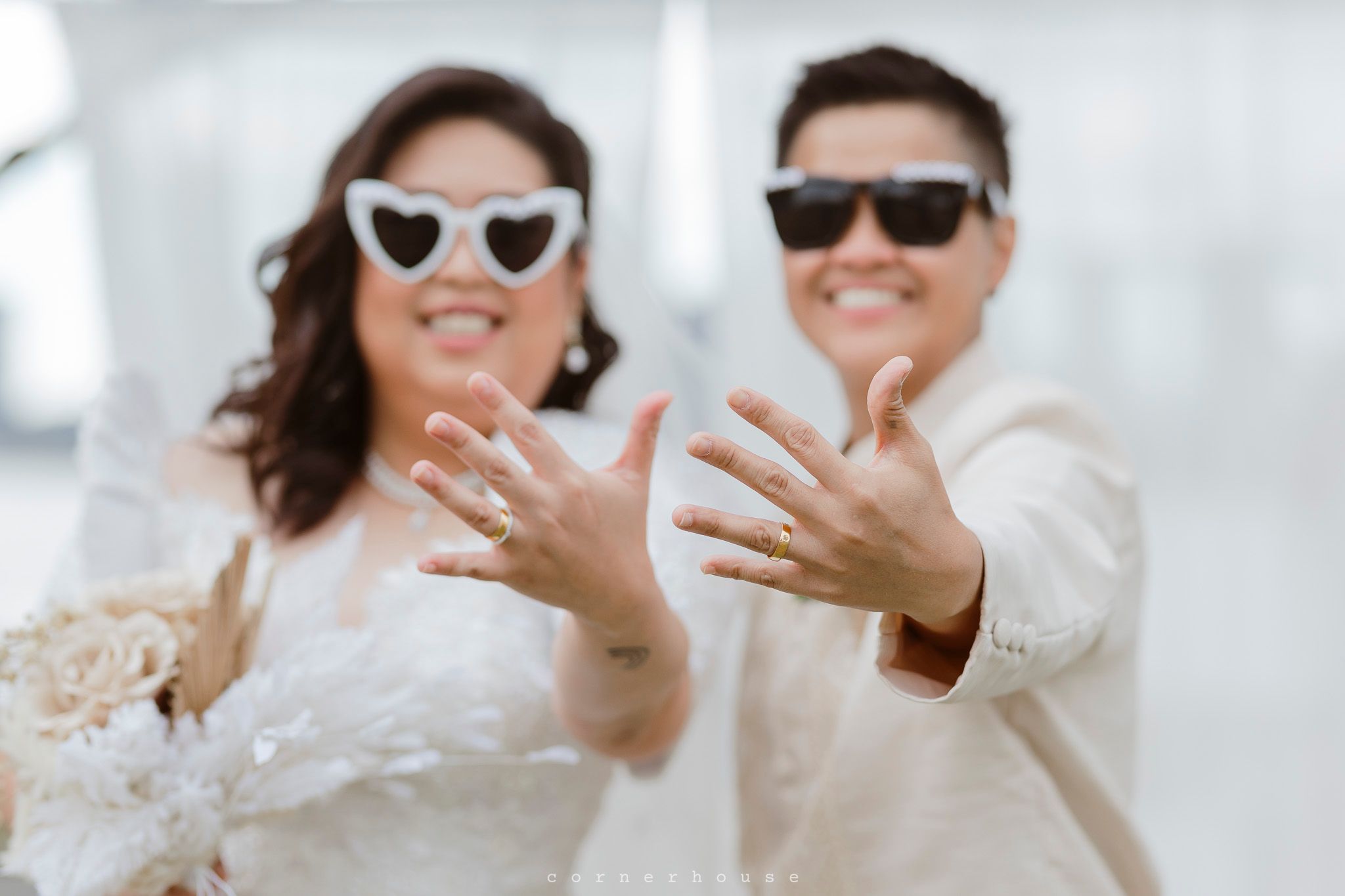 A joyful wedding party wears sunglasses and white attire while laughing and posing together outdoors.
