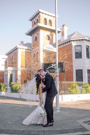 A newlywed couple shares romantic kisses near historic brick buildings and garden arches on their wedding day.