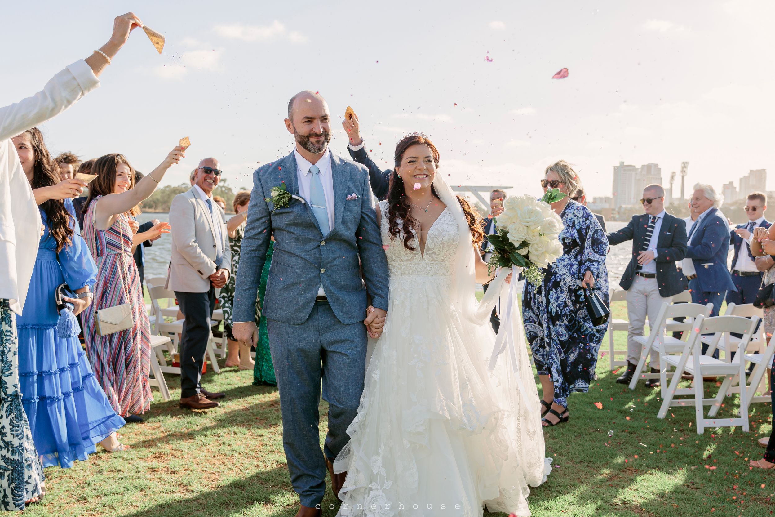Newlyweds walk down the aisle together while guests throw flower petals during an outdoor wedding ceremony.