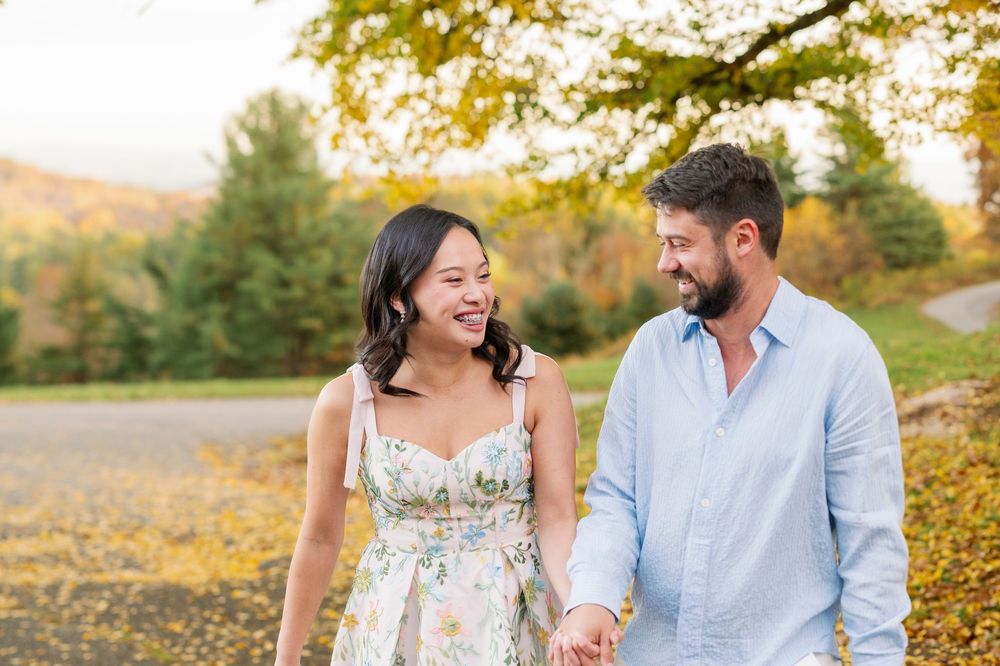 Couple holding hands and smiling at each other outdoors in autumn park with colorful fall foliage.