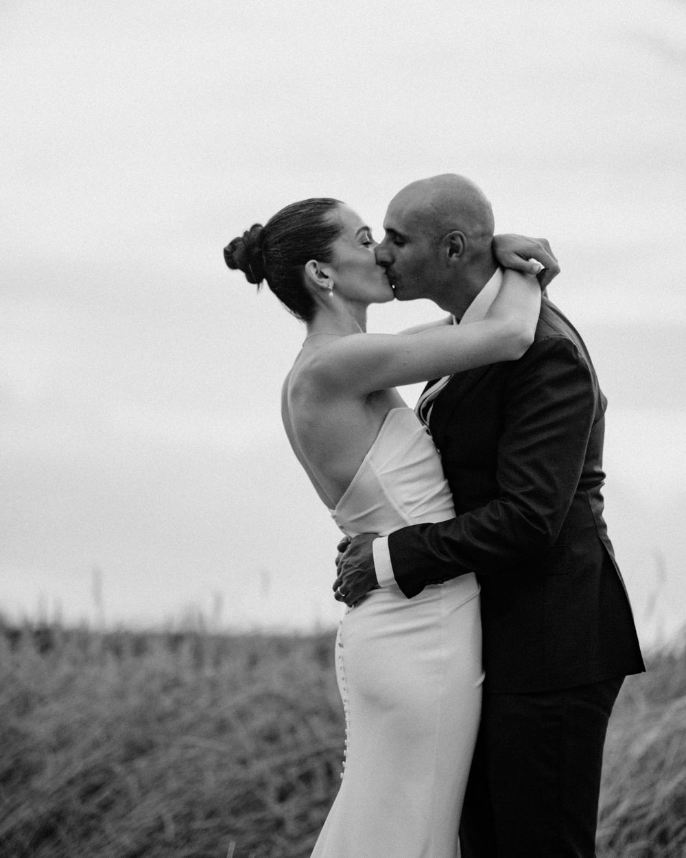 Black and white photo of a couple sharing a romantic kiss outdoors in a field on their wedding day.