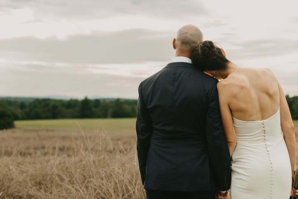 Bride and groom standing together overlooking a golden field on their wedding day.