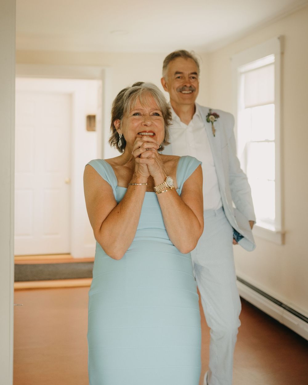 Emotional mother in light blue dress clasping hands with joyful expression at wedding reveal.