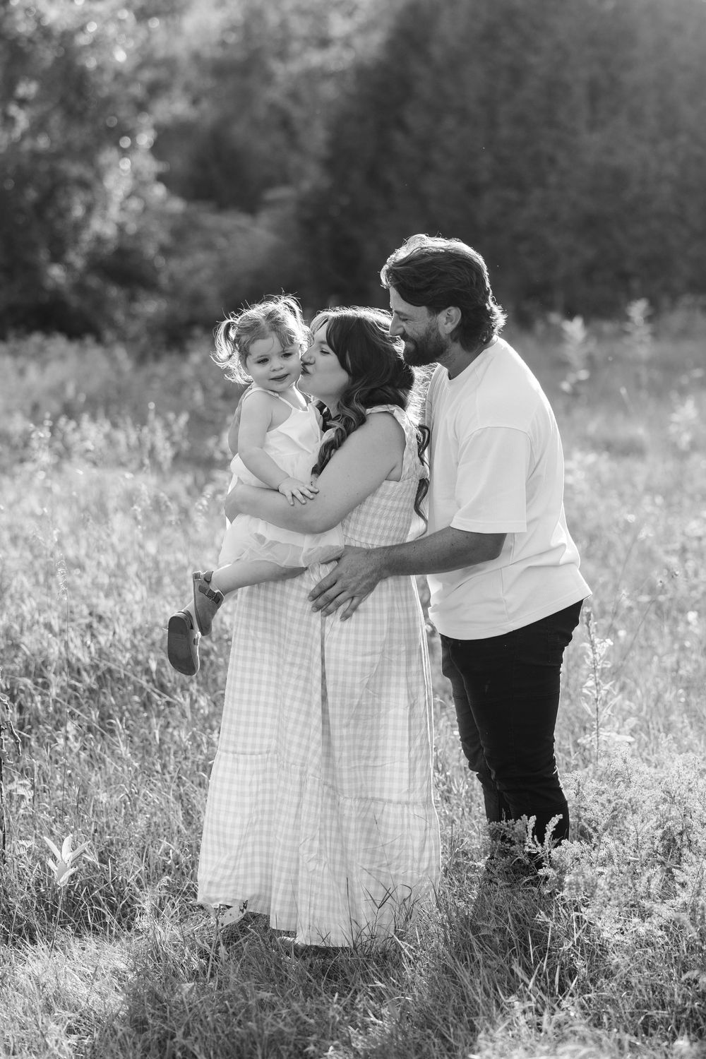 Two young children share a sweet embrace in a sunny summer meadow in black and white.