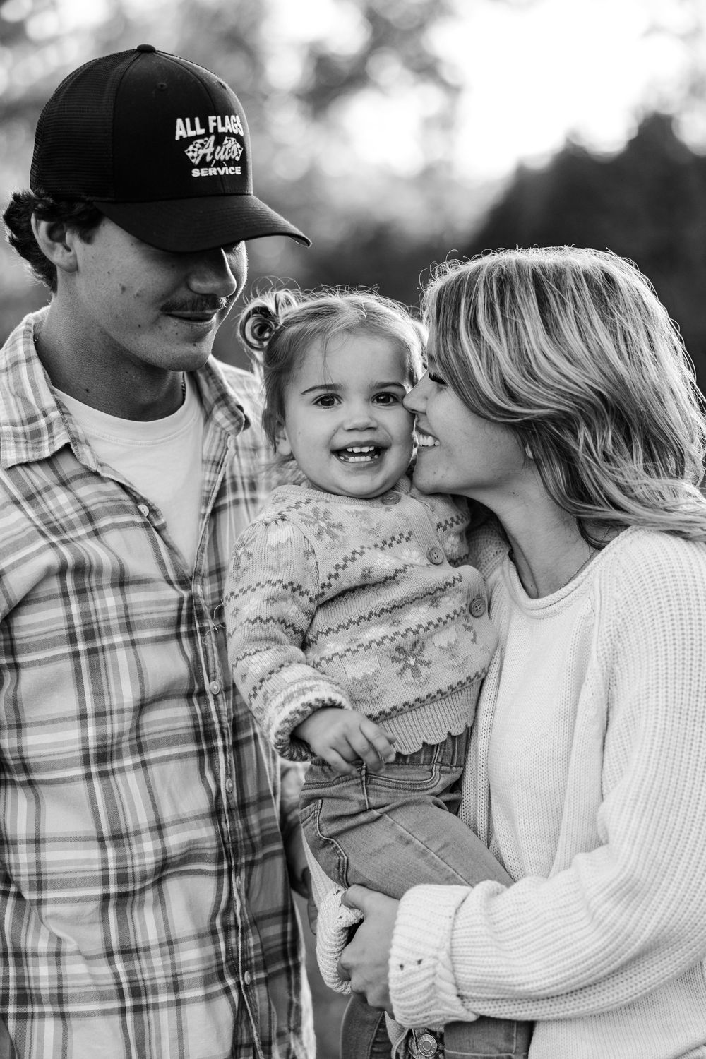 Black and white series of candid family photos showing tender moments in matching white sweaters and plaid shirts.