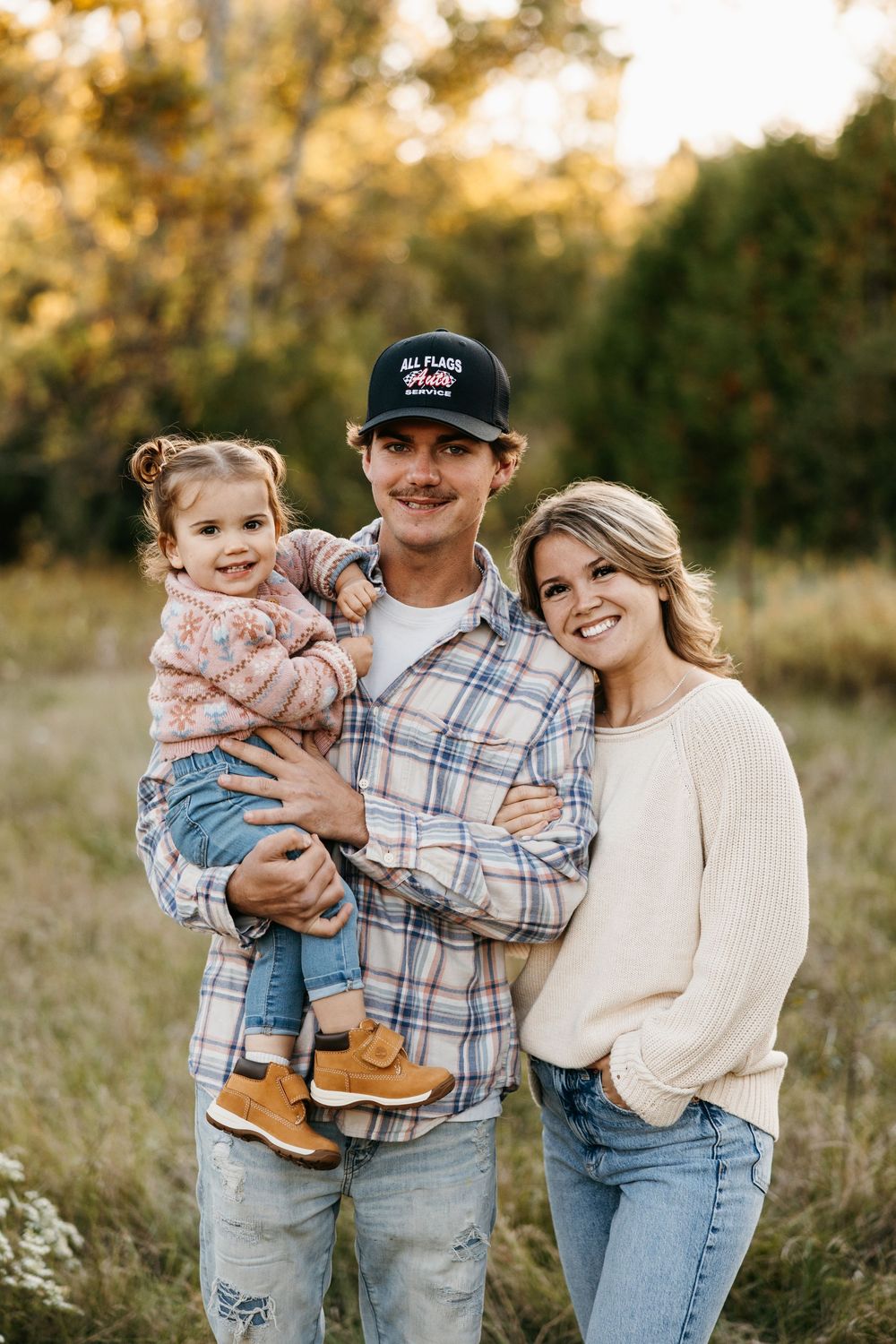 A family poses together outdoors during golden hour in a field with warm autumn lighting and casual attire.