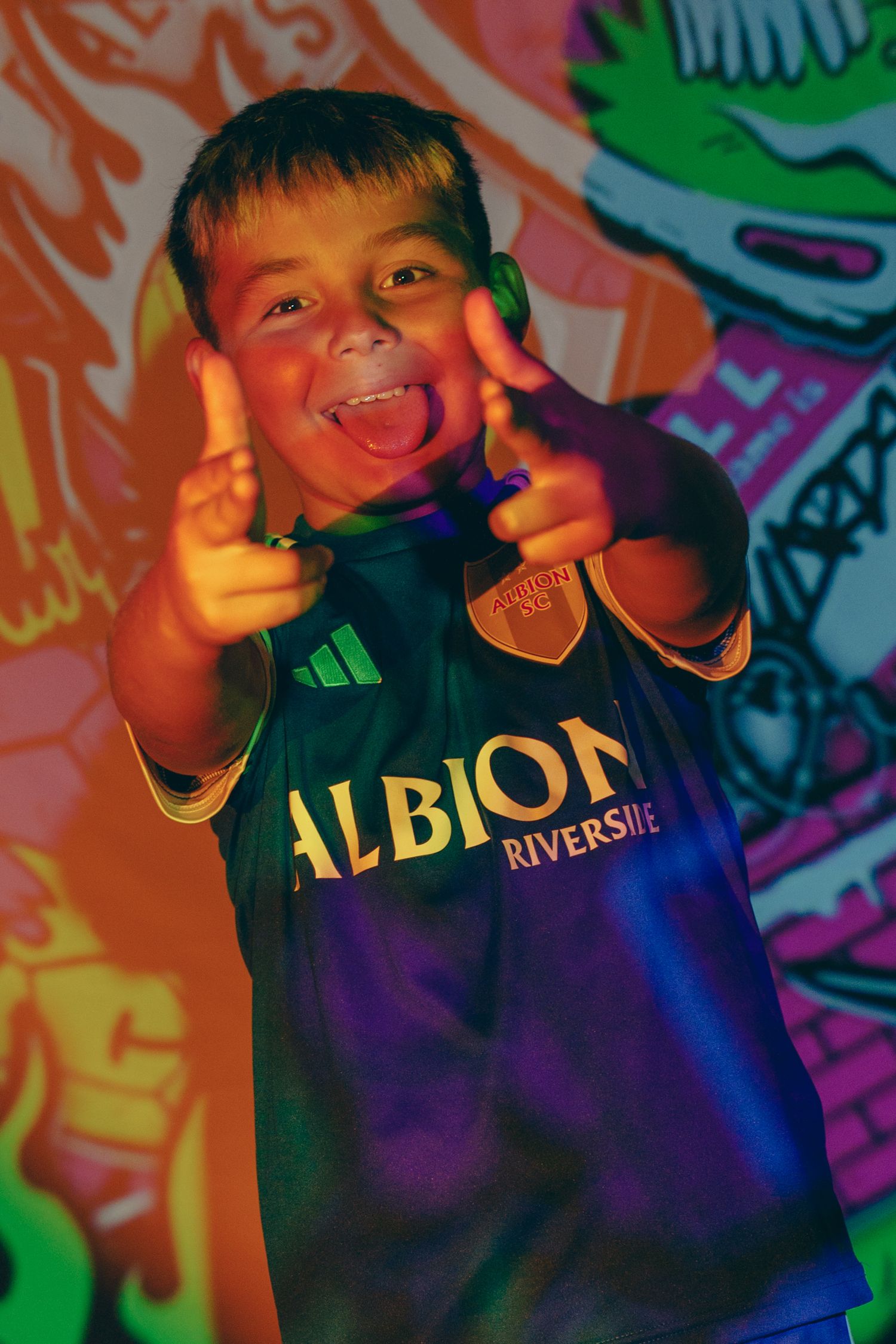 Person wearing Albion shirt poses playfully against colorful graffiti background.
