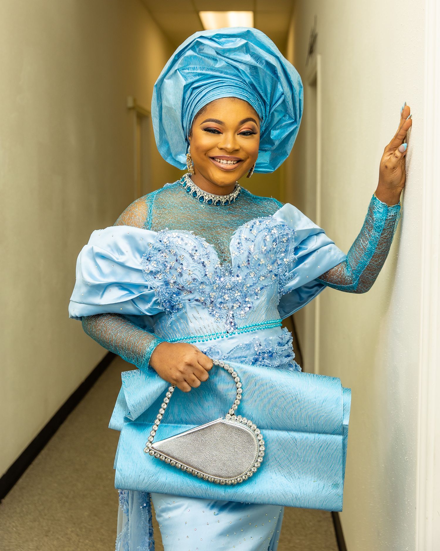 Woman in light blue traditional dress and headwrap smiles at camera.