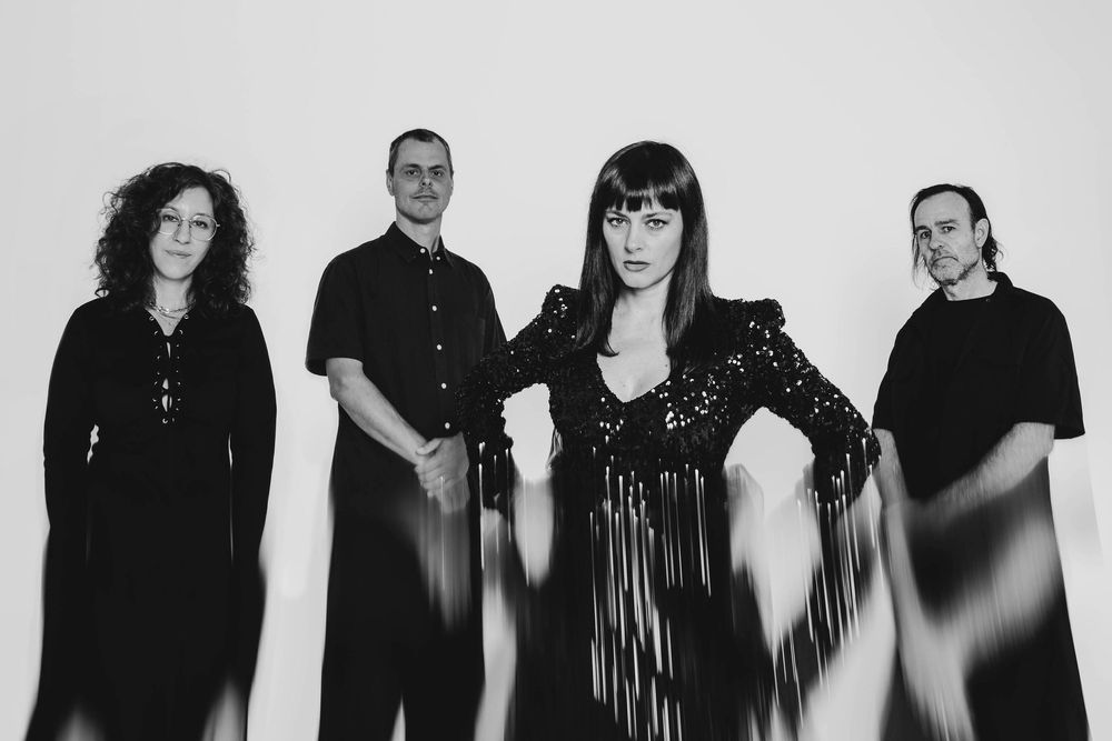 Black and white portrait of four alternative band members dressed in black against a white background.