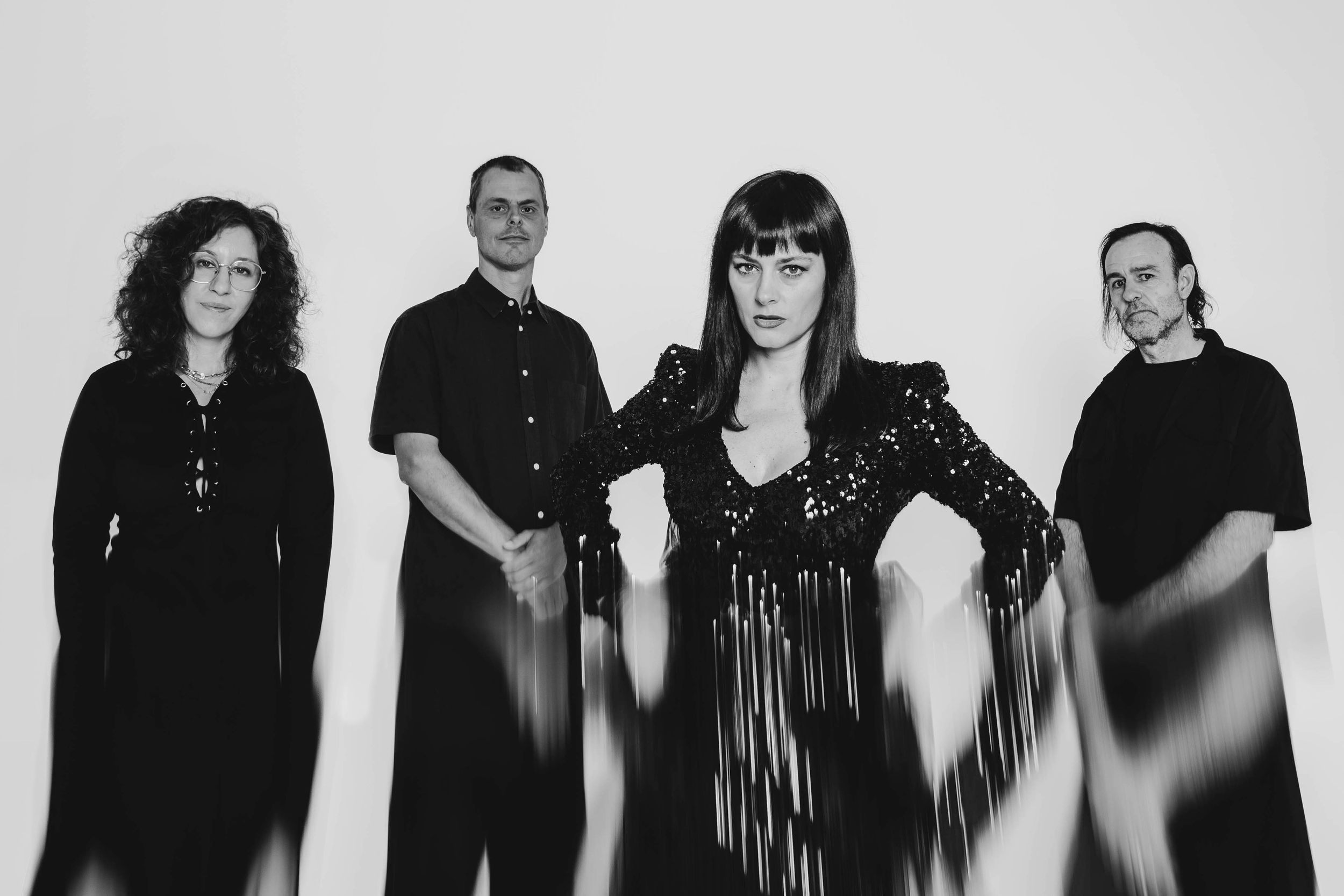 Black and white portrait of four alternative band members dressed in black against a white background.