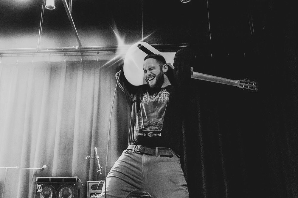 Black and white shot of an energetic rock musician jumping on stage holding a guitar overhead.