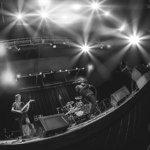 Black and white wide-angle shot of a band performing on stage with bright star-burst stage lighting.
