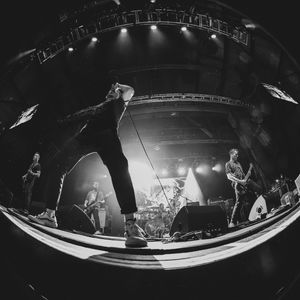 Black and white fisheye photo of a rock band performing with dramatic stage lighting overhead.
