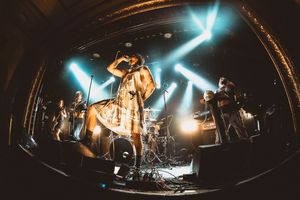 A female singer performs on stage with band under blue stage lights in a fisheye lens concert photo.