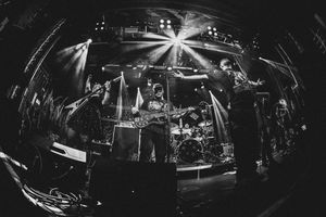 Black and white fisheye shot of a full band performing on stage with dramatic star-burst stage lighting.