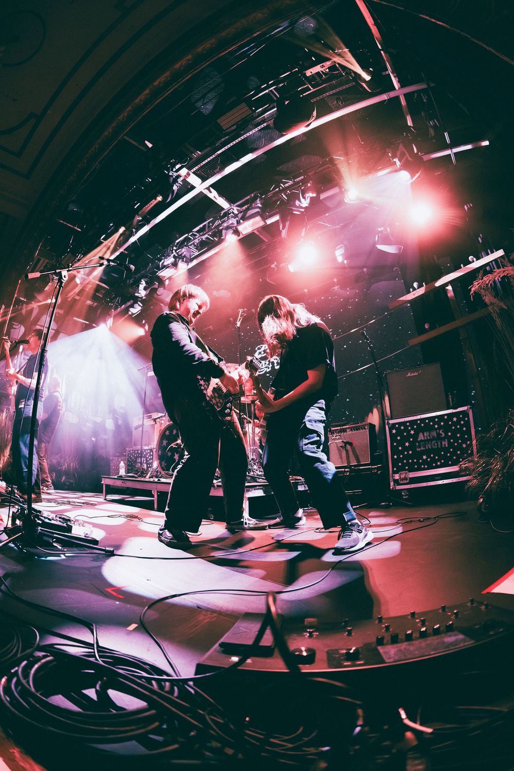 Two guitarists perform on colorful lit stage captured with fisheye lens at a live rock concert.