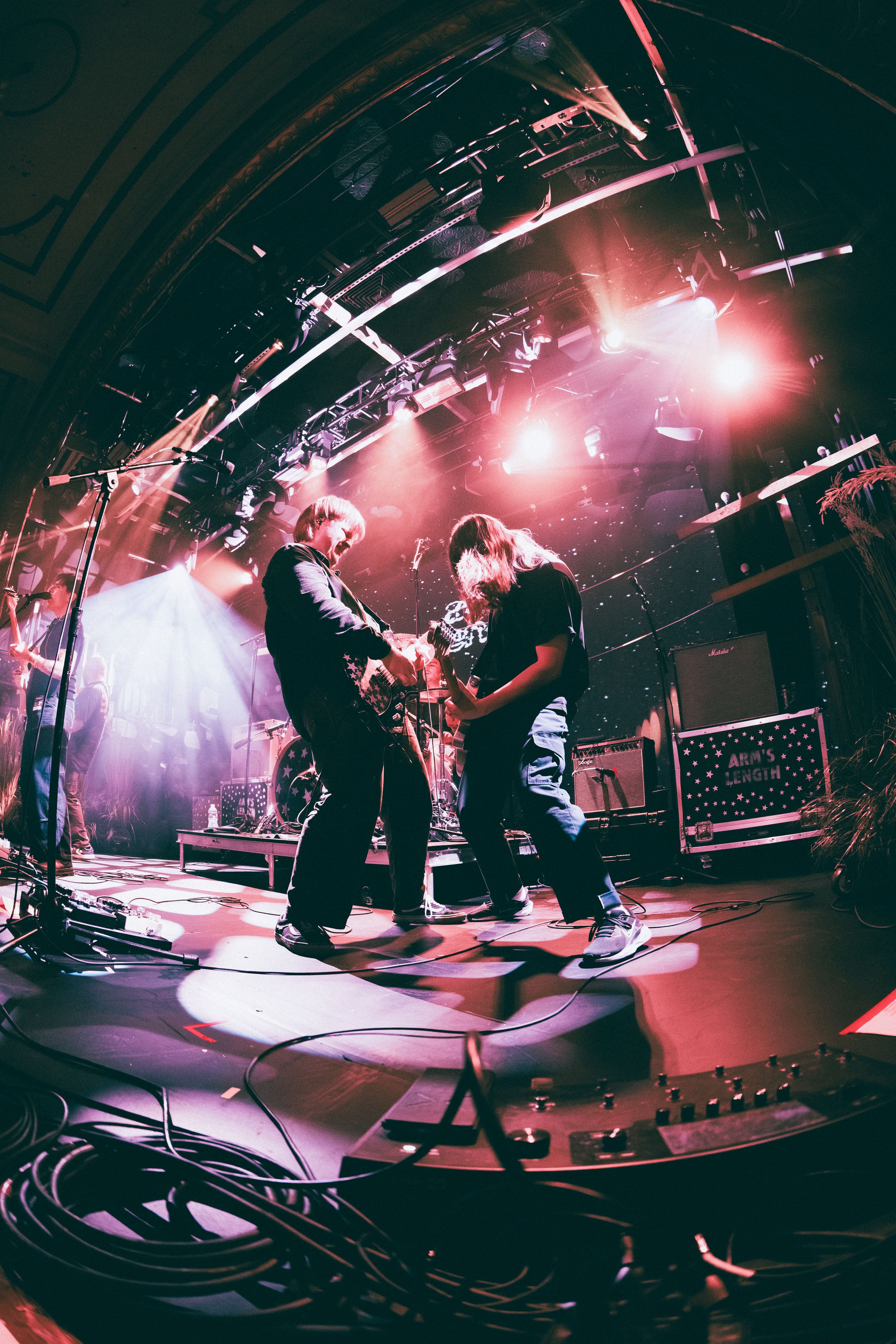 Two guitarists perform on colorful lit stage captured with fisheye lens at a live rock concert.