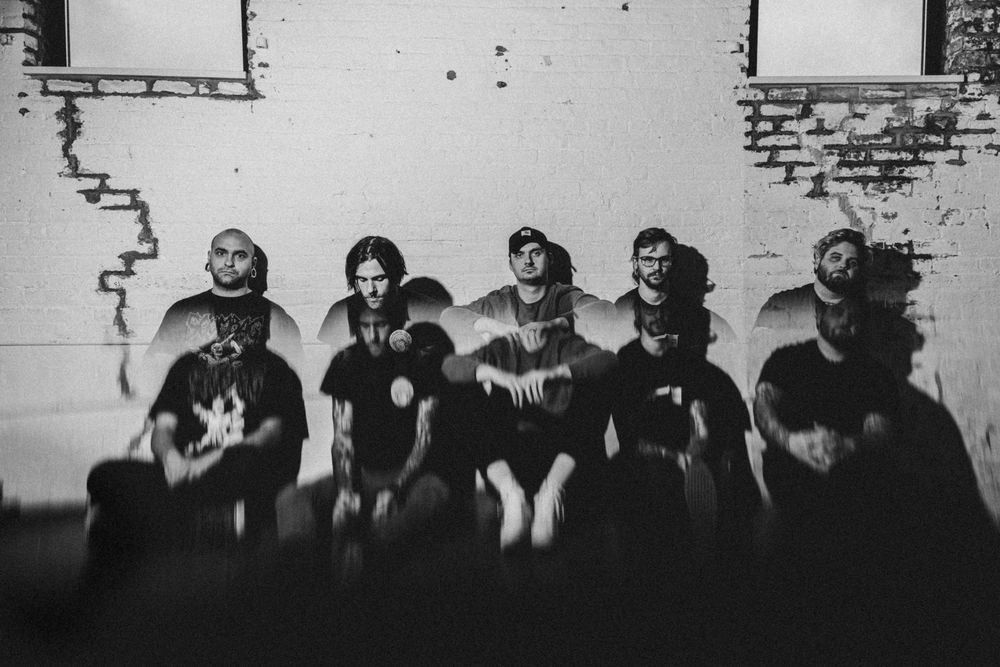 Black and white photo of a heavy metal band posing together against a brick wall in dark graphic tees.