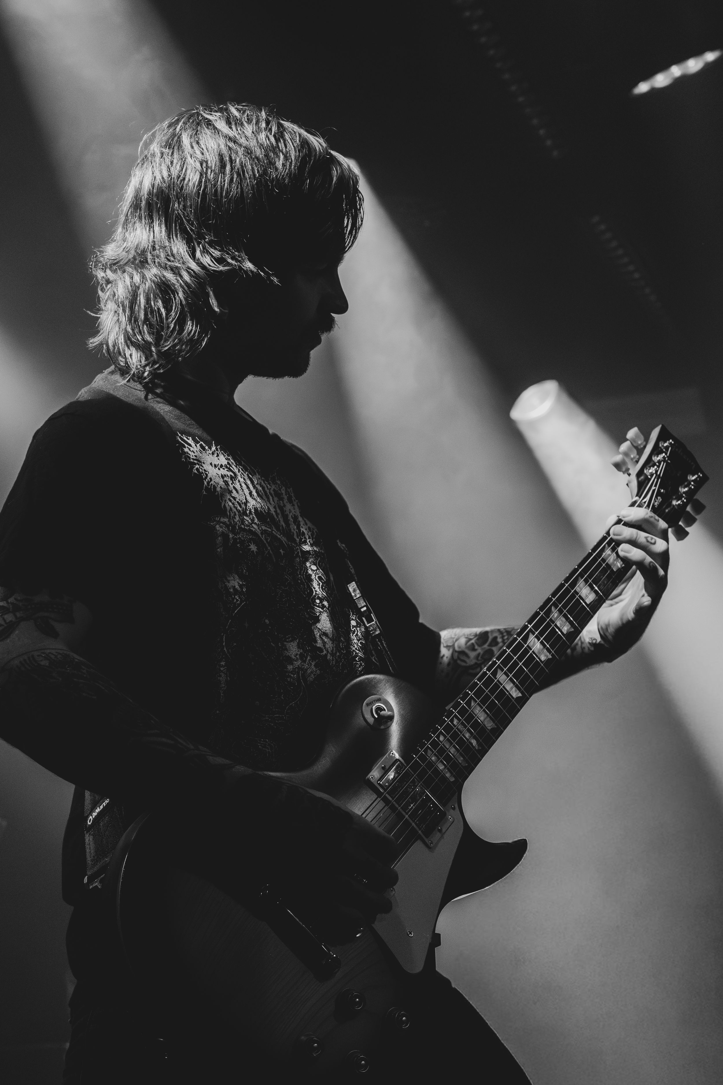 Black and white photo of a guitarist performing on stage under dramatic spotlights during a live concert.