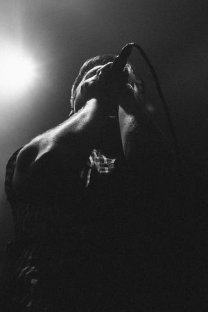 Black and white concert photo of a male singer holding a microphone under dramatic stage lighting.