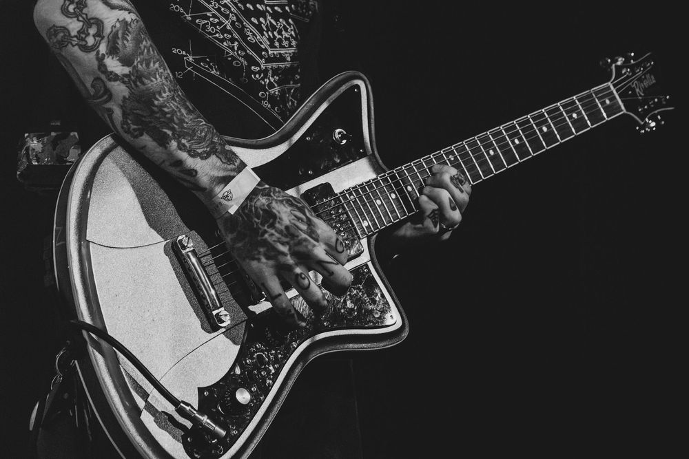 Tattooed musician playing a black and white star-shaped electric guitar in a dramatic black and white photo.