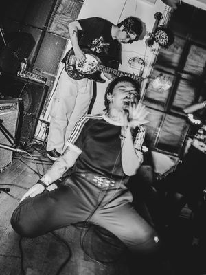 Black and white photo of a rock band performing live, with a vocalist screaming passionately and guitarist playing in the background.