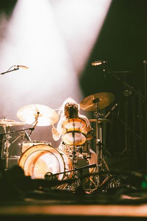 Drummer plays intensely behind a full drum kit bathed in warm golden stage lighting at a live show.
