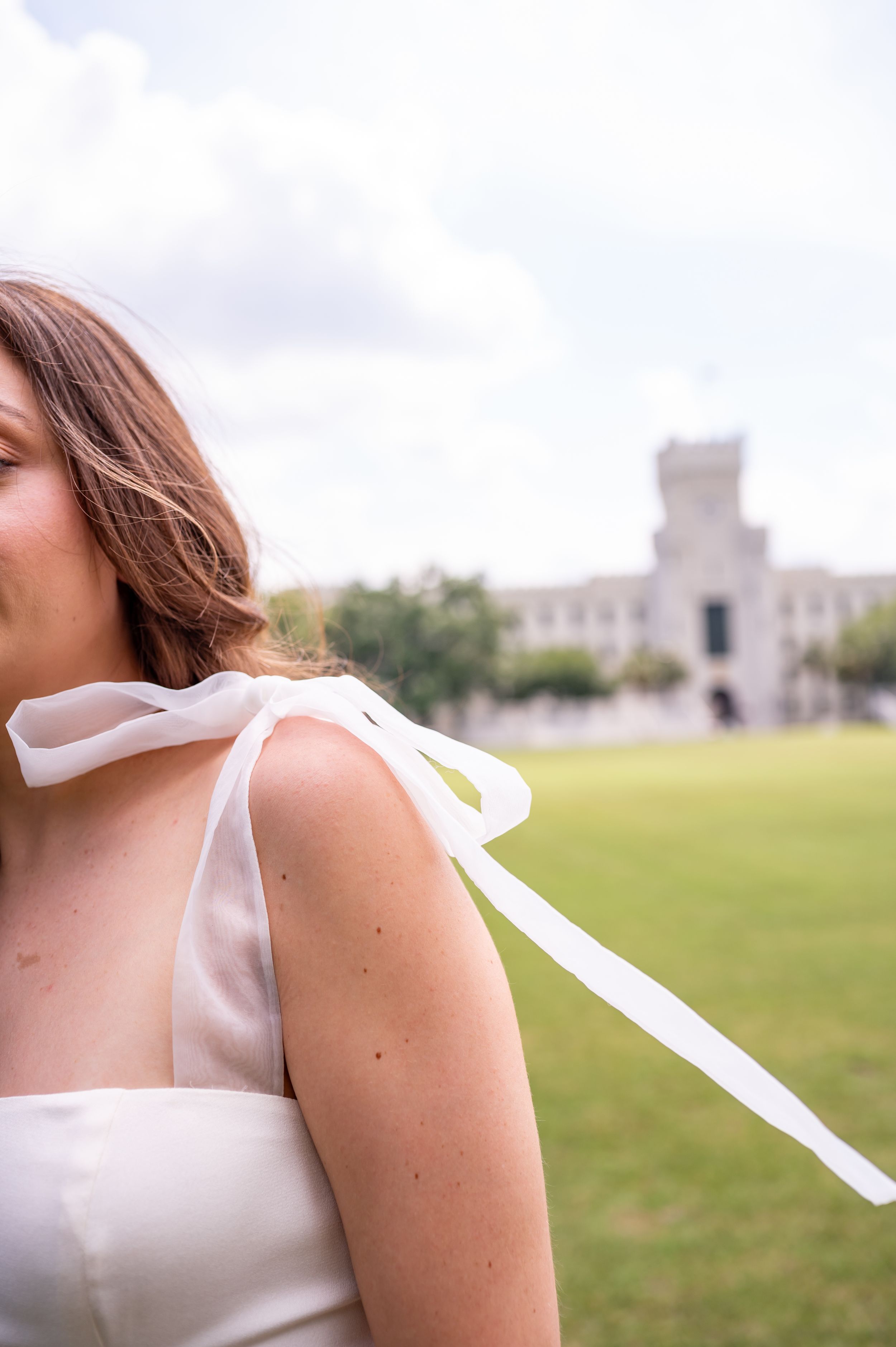 White dress detail with flowing ribbon against a cloudy sky and historic building backdrop.