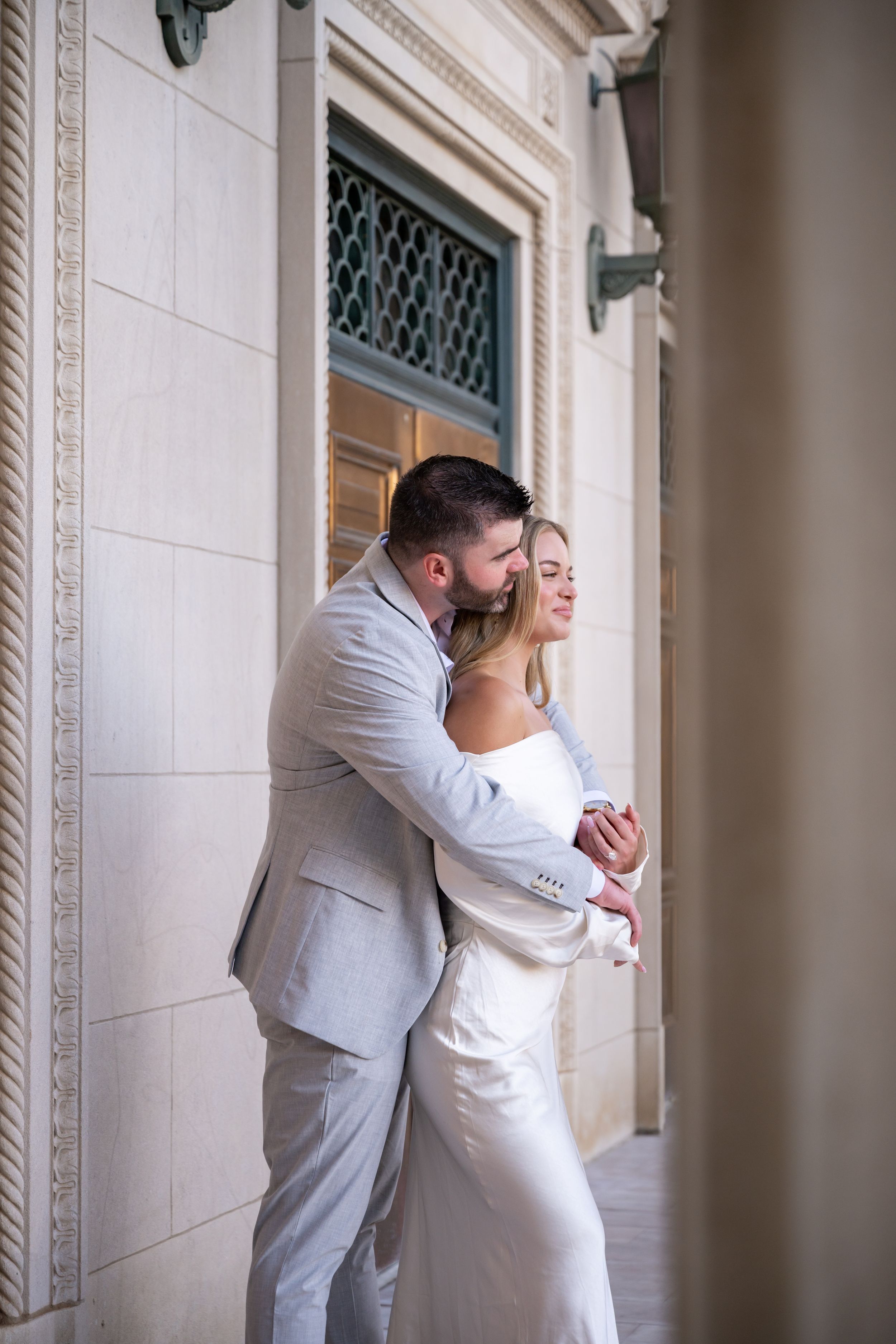 A romantic couple embraces in an elegant hallway with ornate architectural details and soft natural lighting.