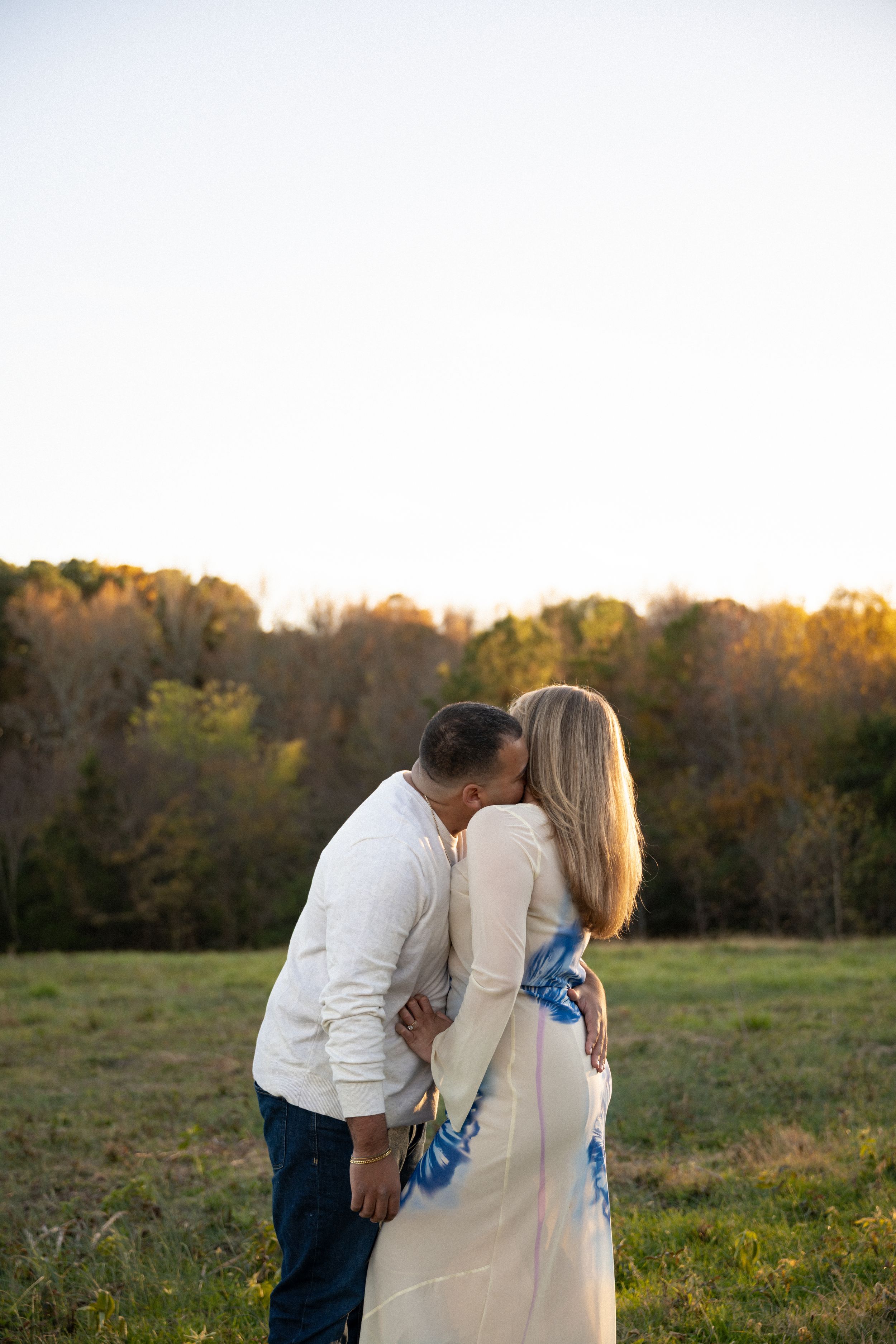 Romantic couple in white clothing share a tender moment in a sunlit autumn field at golden hour.