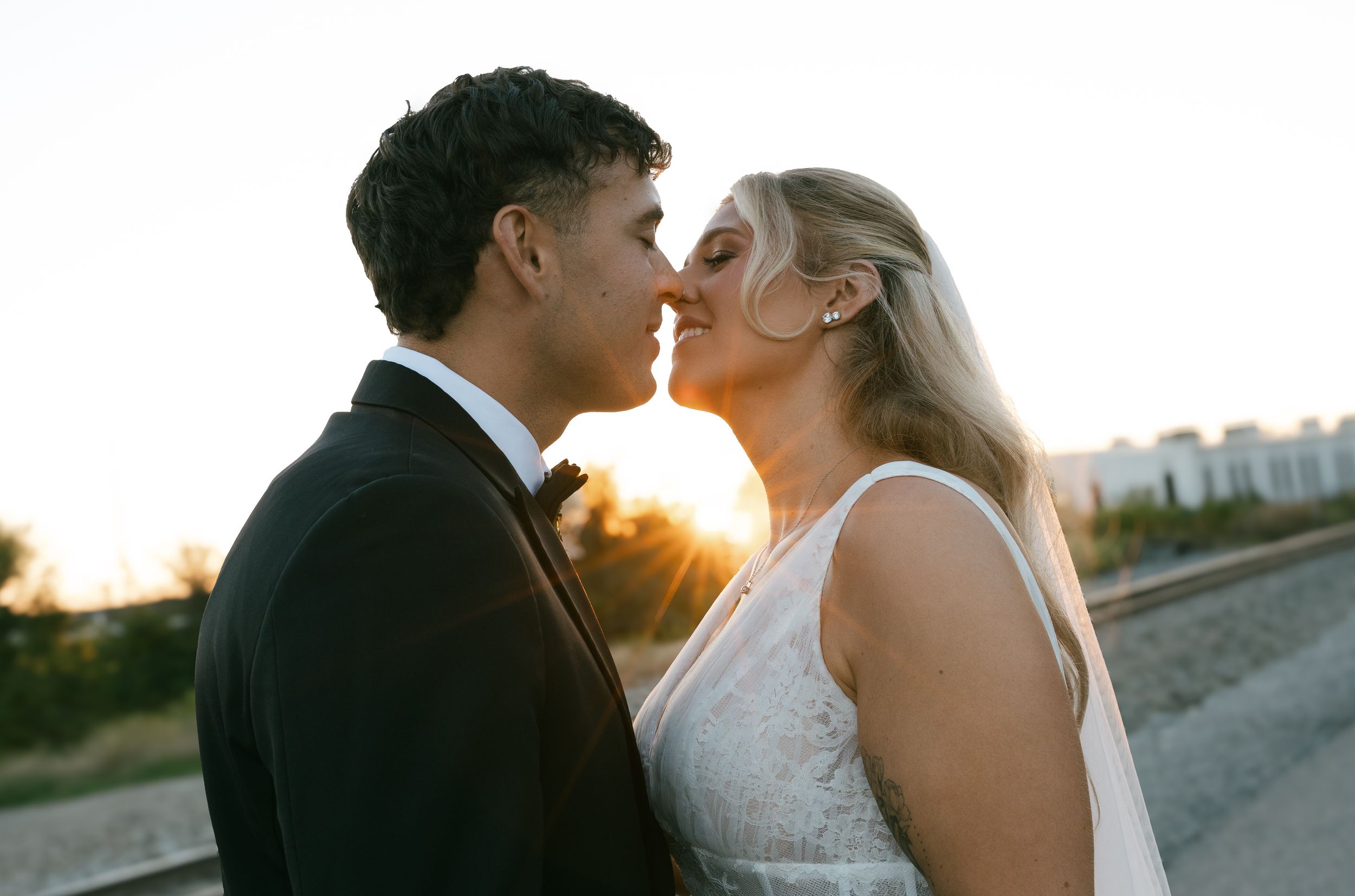 Newlywed couple sharing romantic kiss at night with sparkling lights in background.