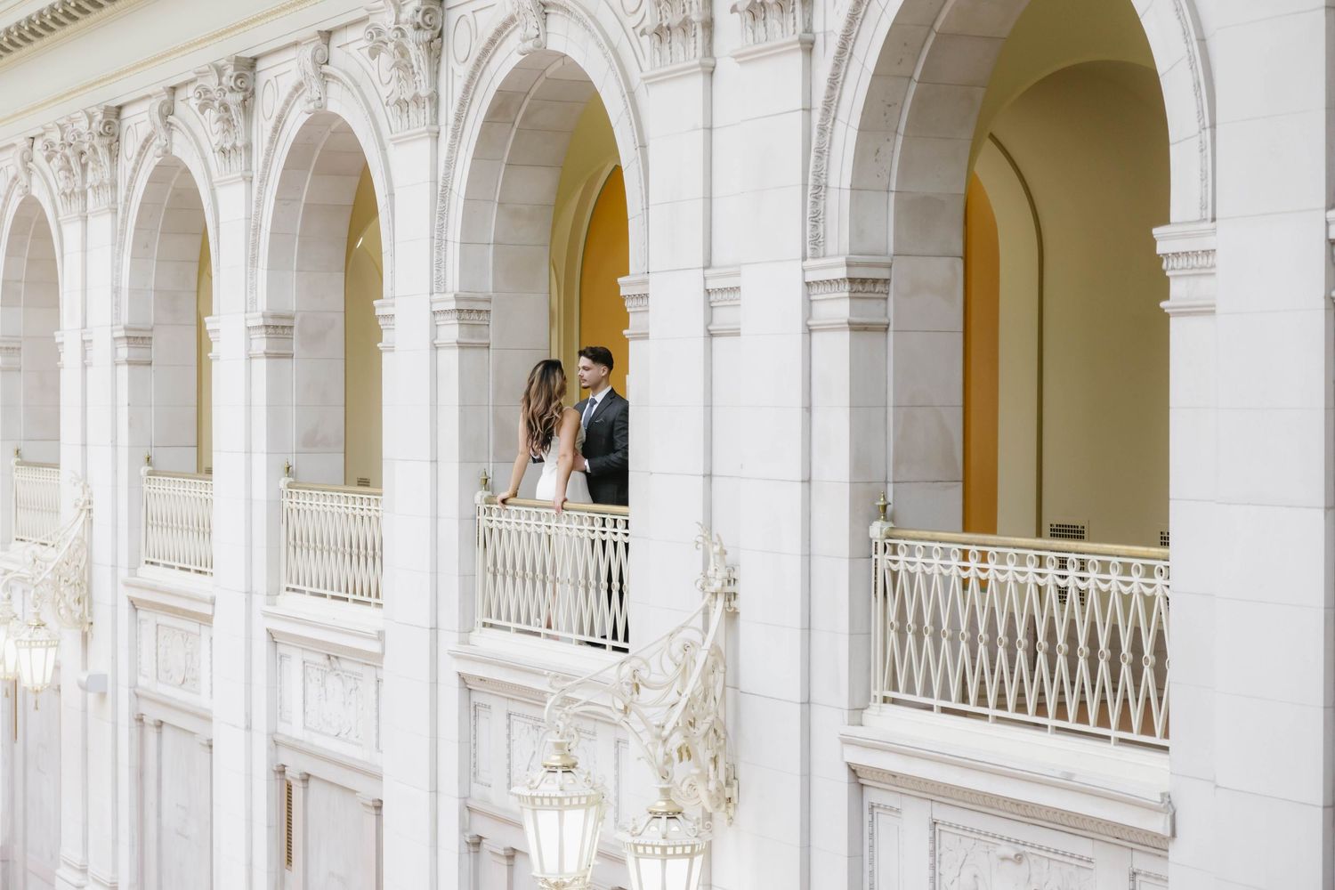 Romantic wedding couple sharing a moment on an elegant white balcony with classical architecture.