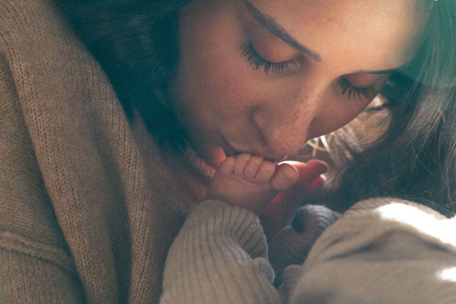 A moody black and white portrait of an expectant mother by a window.