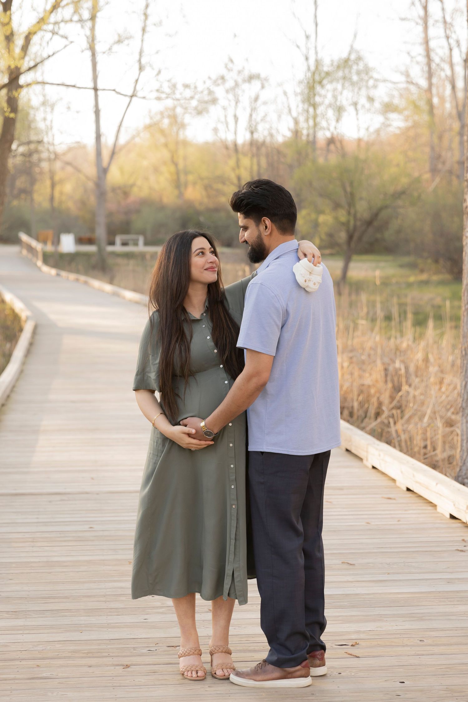 pregnant couple smiling at each other while holding a pair of baby shoes