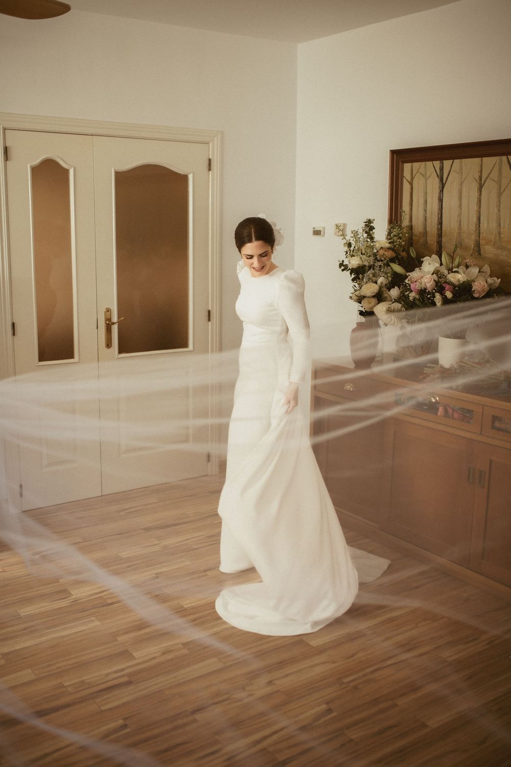 Classic wedding gown with long sleeves and flowing train displayed in an elegant indoor setting with hardwood floors.