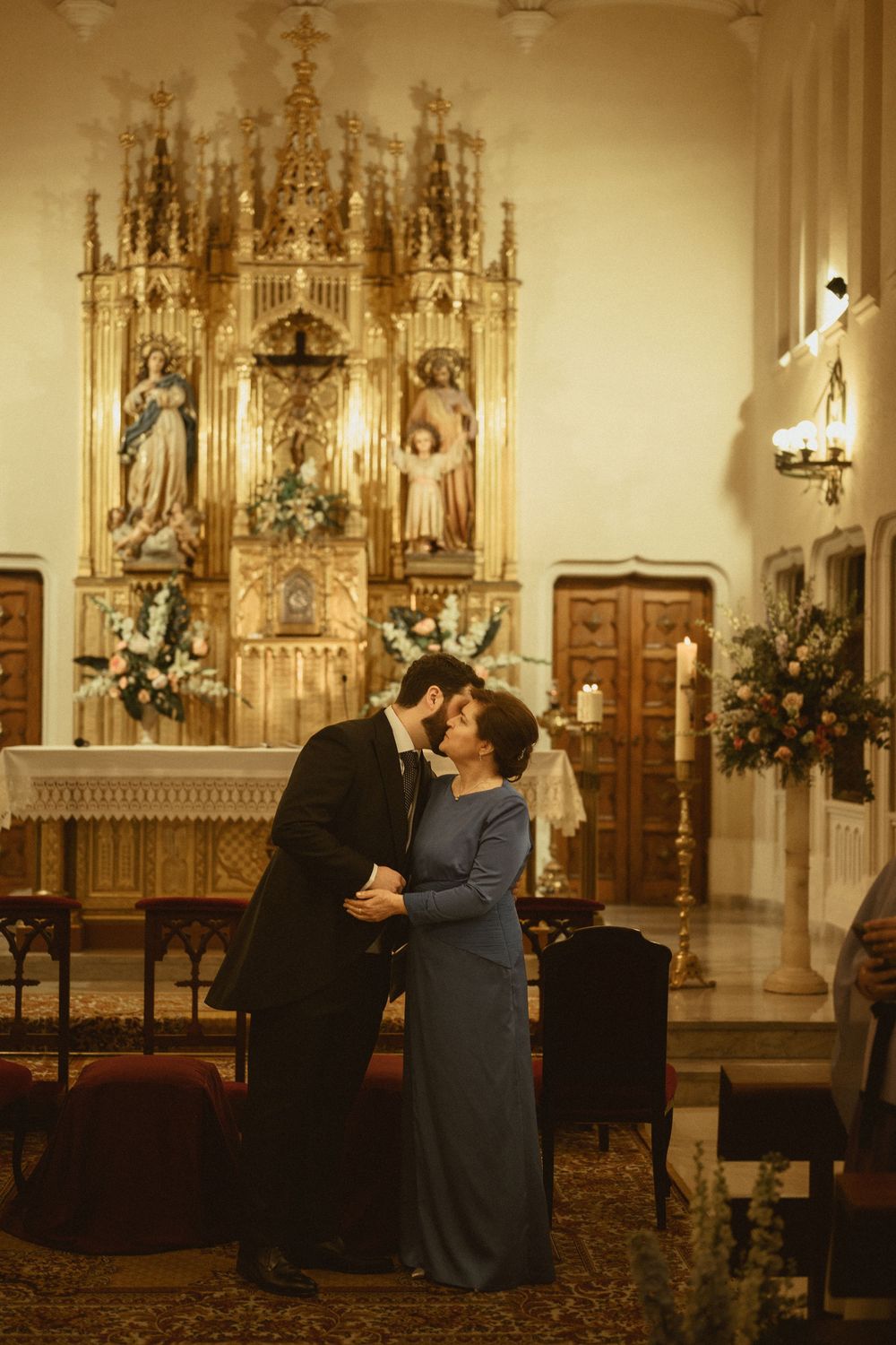 A couple shares an intimate moment in front of an ornate church altar decorated with Gothic architecture.