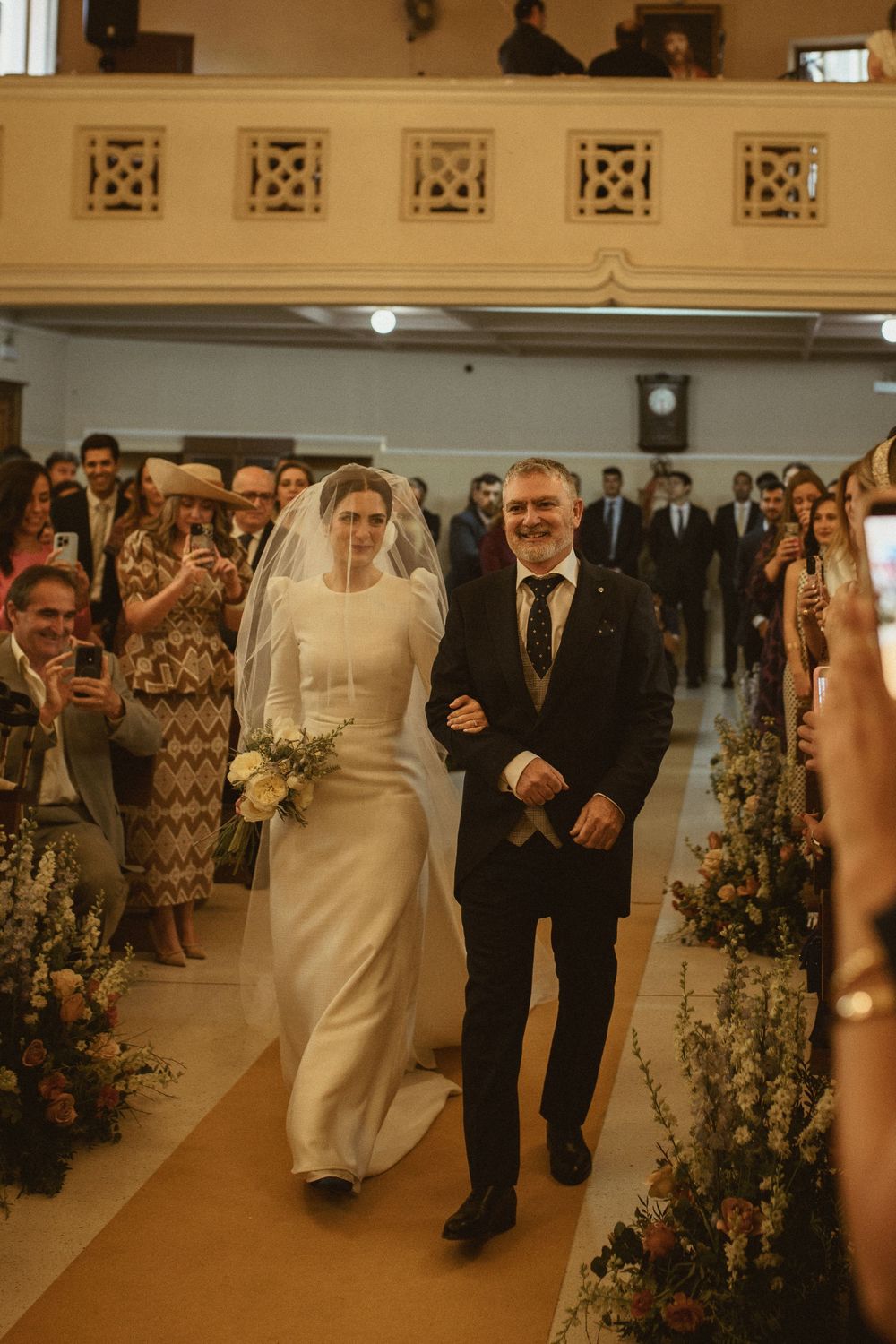 Wedding processional in an ornate church with floral decorations lining the aisle.